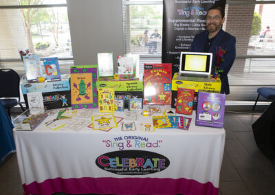 Man posing with children's books on his booth at the Texas Play & Development Conference.