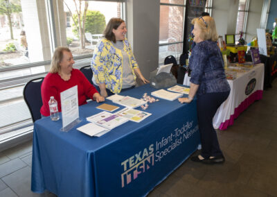 Two women behind a booth speaking to a participant at the Texas Play & Development Conference.
